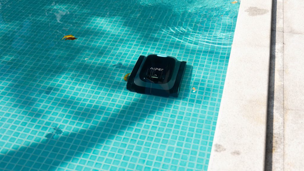 A robotic pool cleaner moving across light blue pool tiles, cleaning debris in the water.