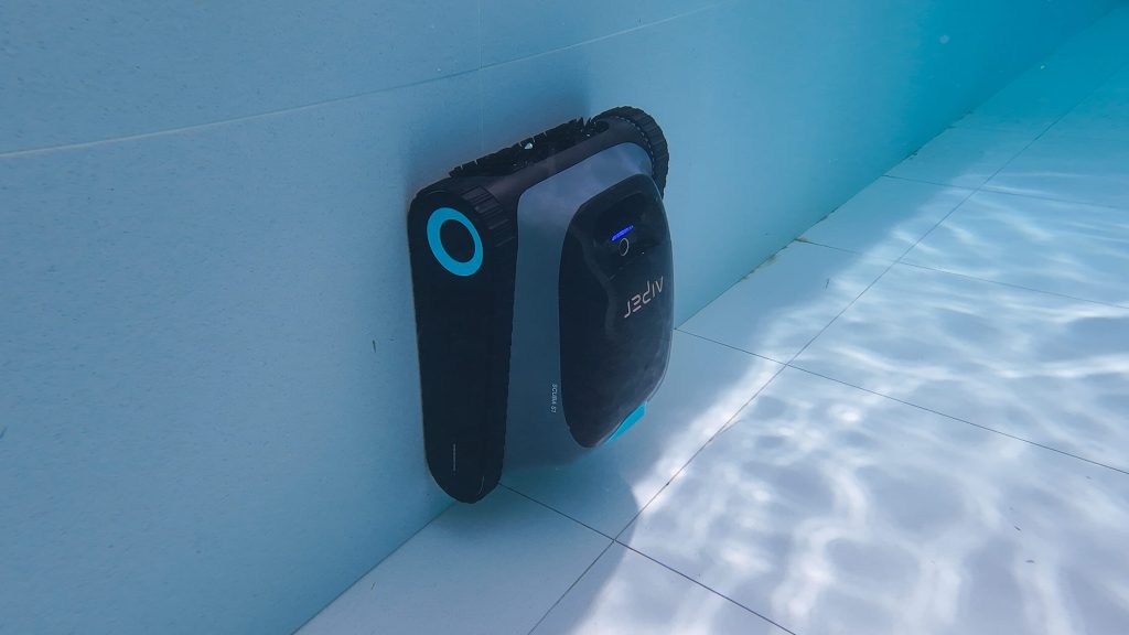 Side view of a robotic pool cleaner resting against the light blue wall of a pool, showing its design and features.