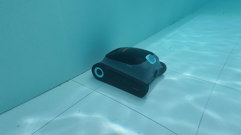 Underwater view of a robotic pool cleaner resting on the tiled floor of a pool, demonstrating its efficiency.