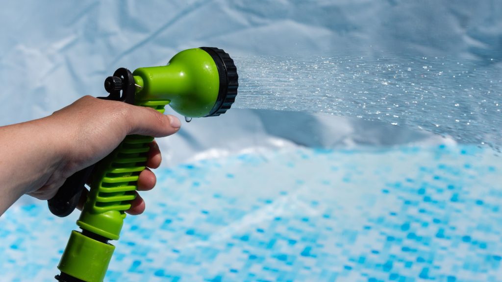 Hand holding a garden hose filling a pool