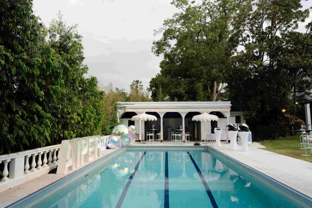 An inviting outdoor swimming pool stretches towards a lounge area shaded by large white umbrellas.