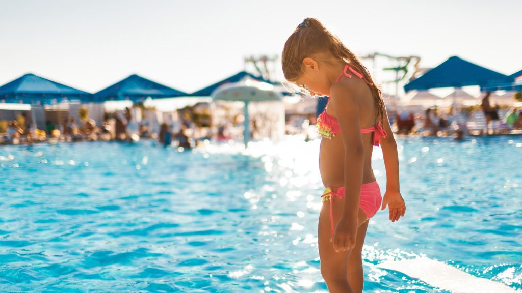 A young girl standing by the pool, contemplating the ideal pool temperature for swimming.